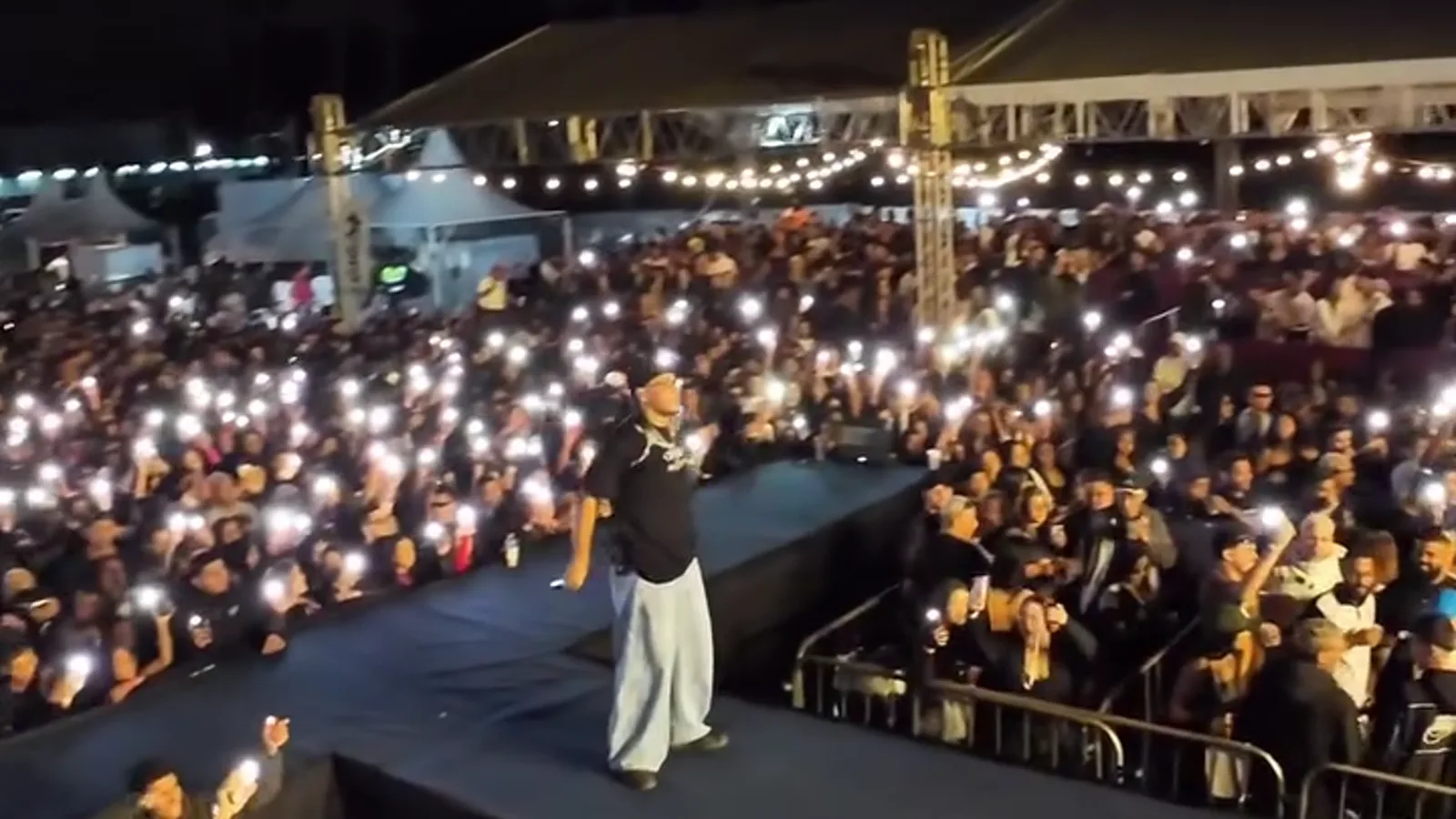 Artista no palco diante do público com as luzes dos celulares acesas