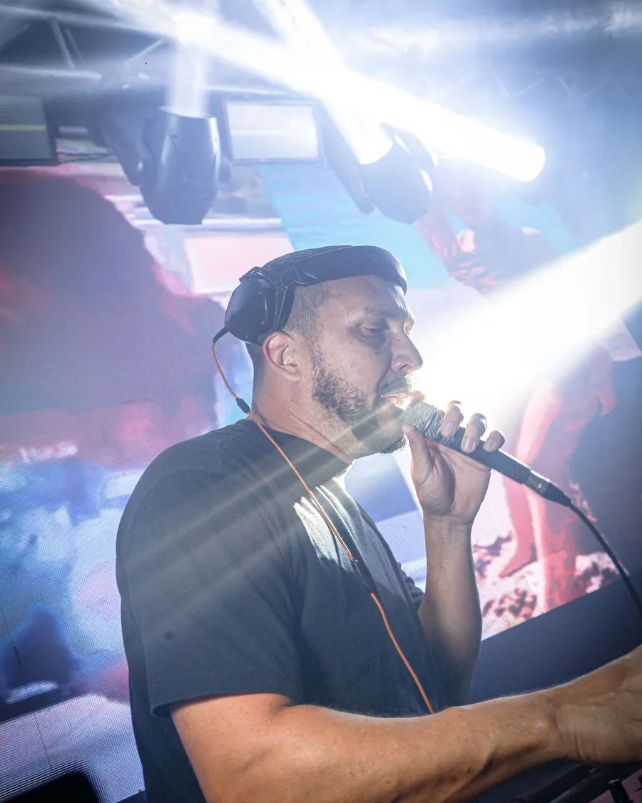 DJ com fone de ouvido comandando a pista diante do painel de LED